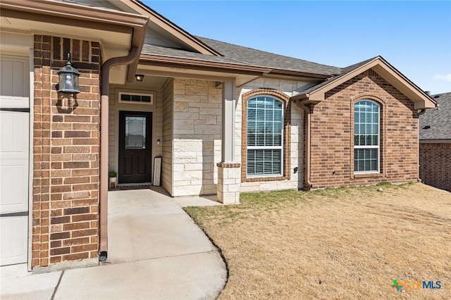 entrance to property with brick siding, stone siding, and a shingled roof