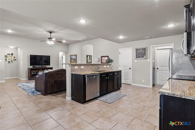 kitchen featuring a ceiling fan, light stone countertops, arched walkways, stainless steel appliances, and open floor plan