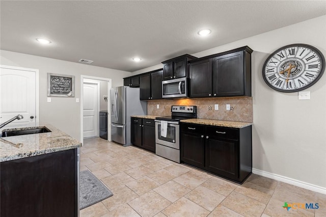 kitchen featuring backsplash, stainless steel appliances, dark cabinetry, and a sink