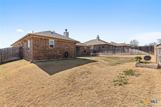 rear view of house featuring a lawn, a fenced backyard, brick siding, and a chimney