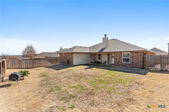 rear view of property featuring a yard, a chimney, a fenced backyard, and brick siding