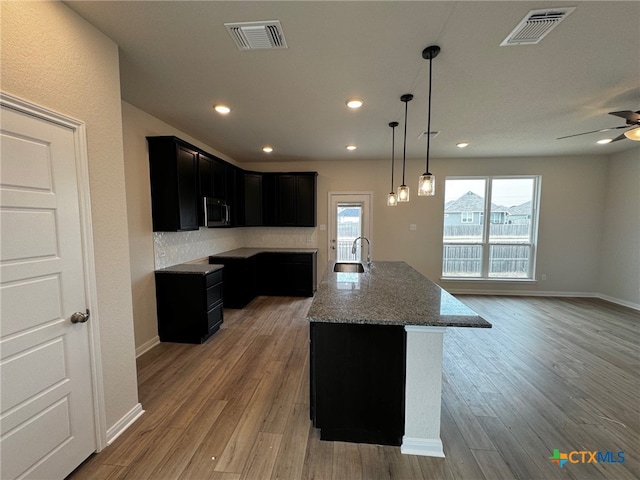 kitchen featuring hardwood / wood-style floors, ceiling fan, a center island with sink, and light stone counters