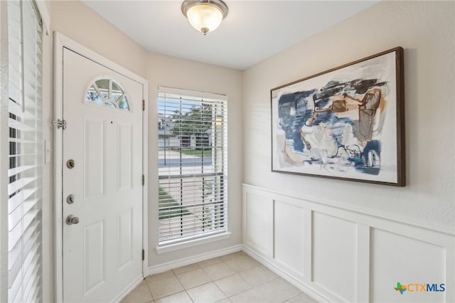 foyer entrance with wainscoting, a decorative wall, and light tile patterned floors