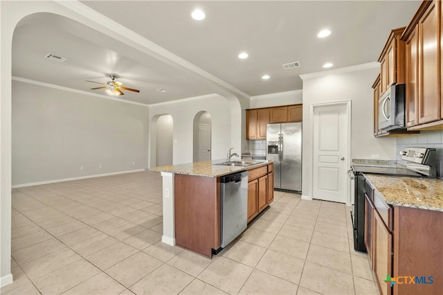 kitchen featuring tasteful backsplash, light stone countertops, a center island with sink, and appliances with stainless steel finishes