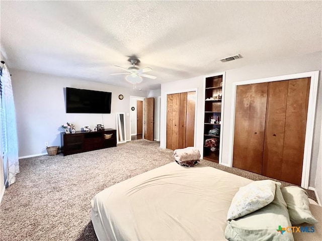 bedroom featuring carpet floors, ceiling fan, a textured ceiling, and two closets