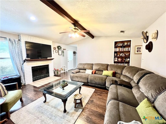 living room with a textured ceiling, ceiling fan, a brick fireplace, lofted ceiling with beams, and dark wood-type flooring