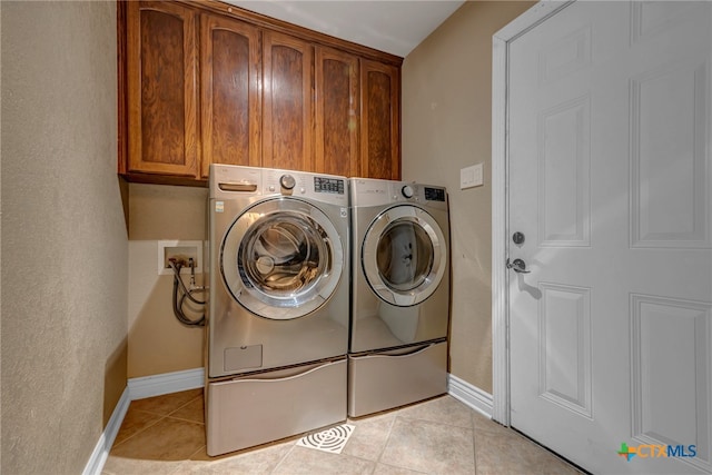 clothes washing area featuring cabinets, light tile patterned floors, and washing machine and clothes dryer