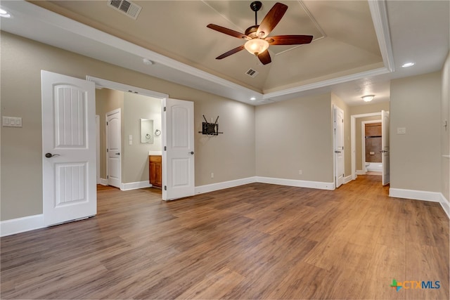 interior space with a raised ceiling, ensuite bathroom, ceiling fan, and light hardwood / wood-style floors