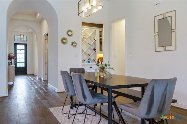 dining room with dark wood-type flooring, arched walkways, and baseboards