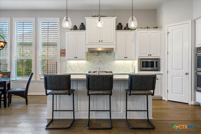 kitchen with dark wood-style flooring, an island with sink, white cabinets, backsplash, and stainless steel appliances