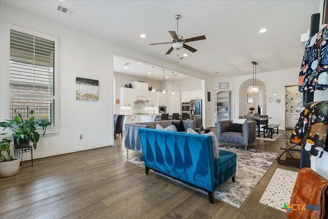 living area featuring visible vents, arched walkways, ceiling fan, and wood finished floors