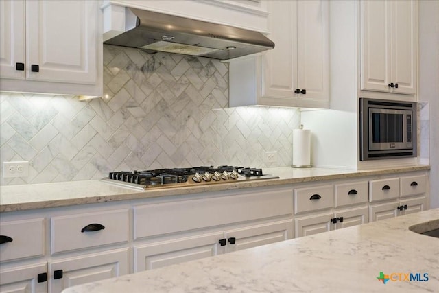 kitchen with appliances with stainless steel finishes, light stone counters, white cabinetry, decorative backsplash, and range hood