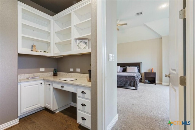 unfurnished office featuring visible vents, built in study area, baseboards, dark carpet, and ceiling fan