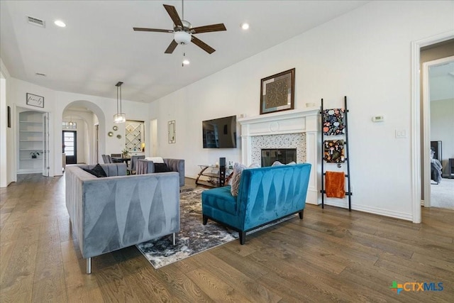 living area with visible vents, wood finished floors, ceiling fan, a tiled fireplace, and arched walkways