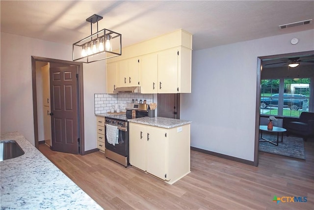 1317 N 10th St, Temple, TX 76501 - kitchen with stainless steel electric stove, under cabinet range hood, light wood-style flooring, tasteful backsplash, and a chandelier