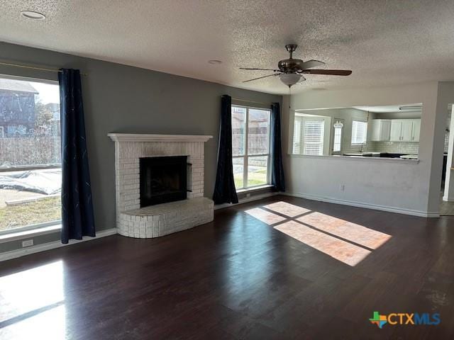 unfurnished living room featuring a wealth of natural light, ceiling fan, dark wood-type flooring, and a textured ceiling