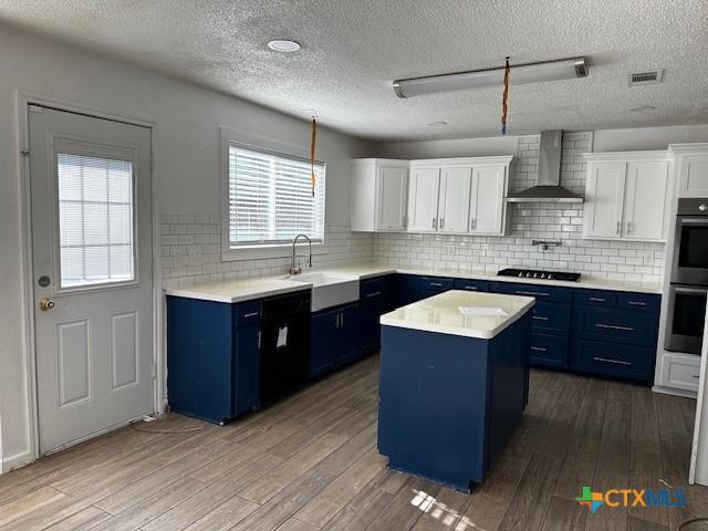 kitchen featuring white cabinets, a center island, wall chimney range hood, and sink