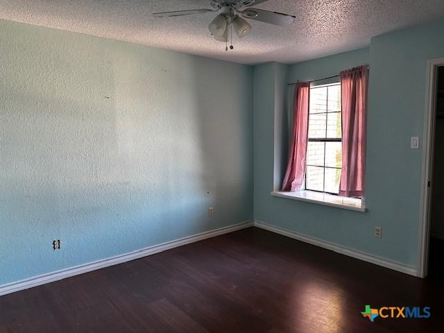 empty room with ceiling fan, dark wood-type flooring, and a textured ceiling