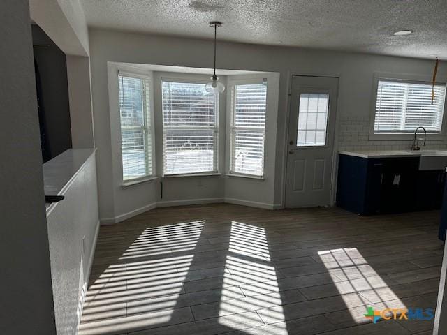 unfurnished dining area featuring a textured ceiling, dark hardwood / wood-style flooring, a wealth of natural light, and sink