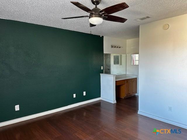 empty room with ceiling fan, a textured ceiling, and dark wood-type flooring