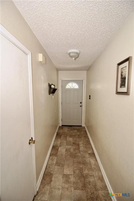 doorway to outside featuring a textured ceiling, baseboards, and stone finish flooring