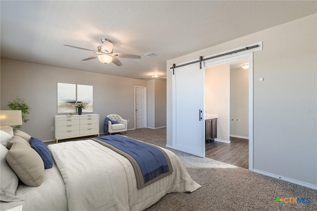 carpeted bedroom with a barn door, baseboards, visible vents, and ceiling fan