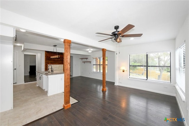 unfurnished living room featuring a ceiling fan, wood finished floors, baseboards, decorative columns, and a sink