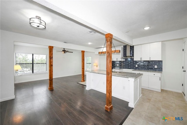 kitchen with visible vents, white cabinetry, wall chimney range hood, decorative backsplash, and light stone countertops