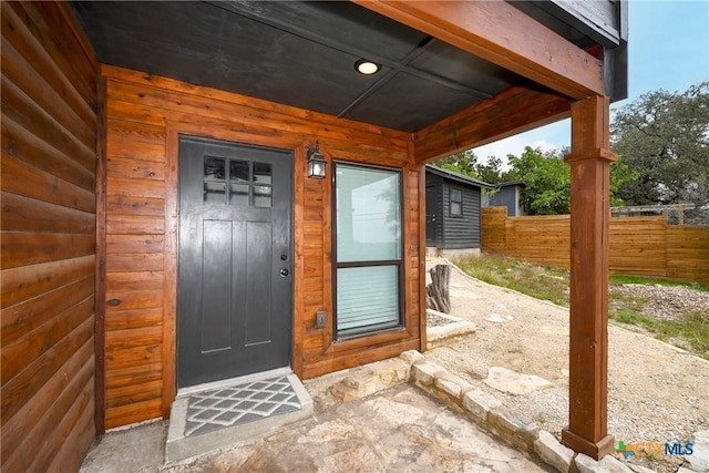 view of exterior entry featuring faux log siding and fence