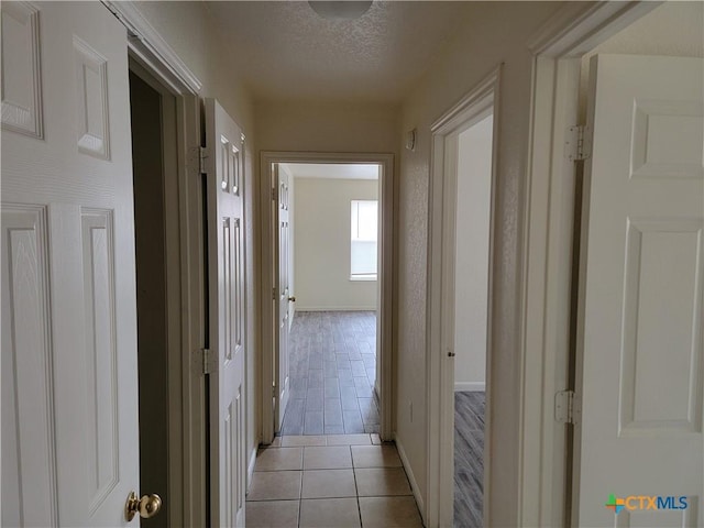 hallway with light tile patterned floors, baseboards, and a textured ceiling