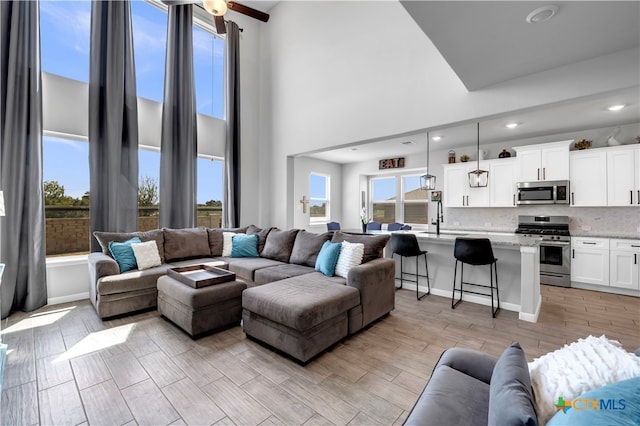 living room featuring a towering ceiling, sink, and light wood-type flooring