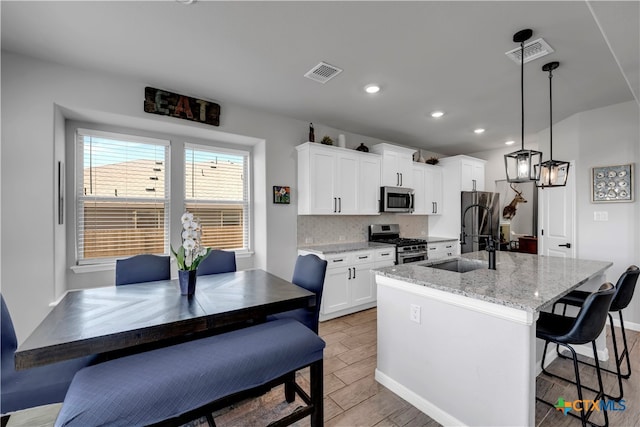 kitchen with stainless steel appliances, light stone countertops, an island with sink, white cabinets, and pendant lighting