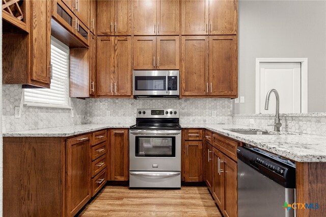 152 Navarro Xing Unit 3B, Seguin, TX 78155 - kitchen featuring stainless steel appliances, a peninsula, light stone counters, brown cabinetry, and tasteful backsplash