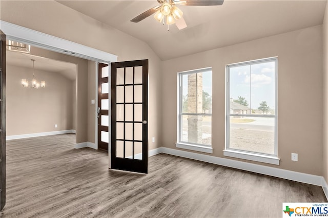 empty room featuring hardwood / wood-style flooring, ceiling fan with notable chandelier, and vaulted ceiling