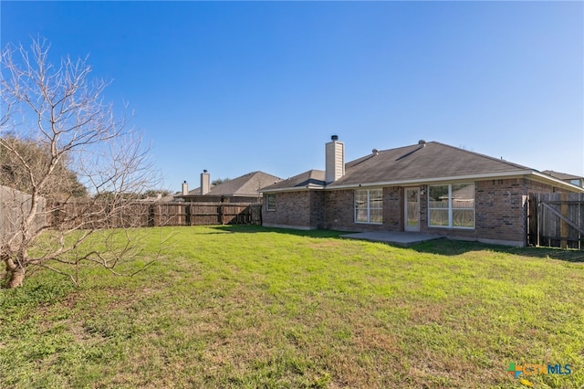 rear view of house featuring a patio, a fenced backyard, a chimney, brick siding, and a lawn
