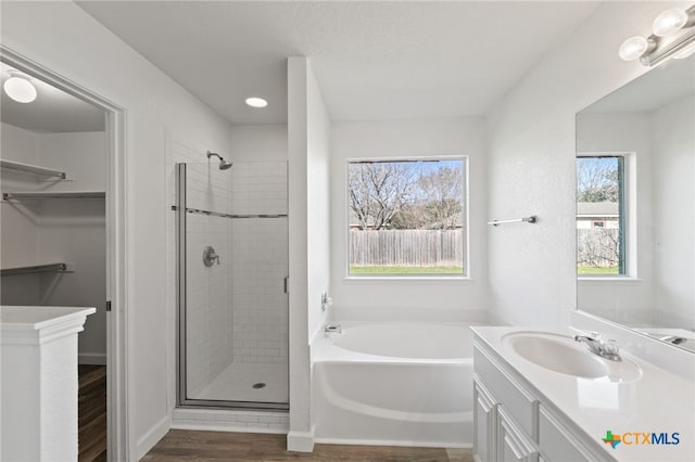 bathroom featuring a walk in closet, a bath, a shower stall, wood finished floors, and vanity