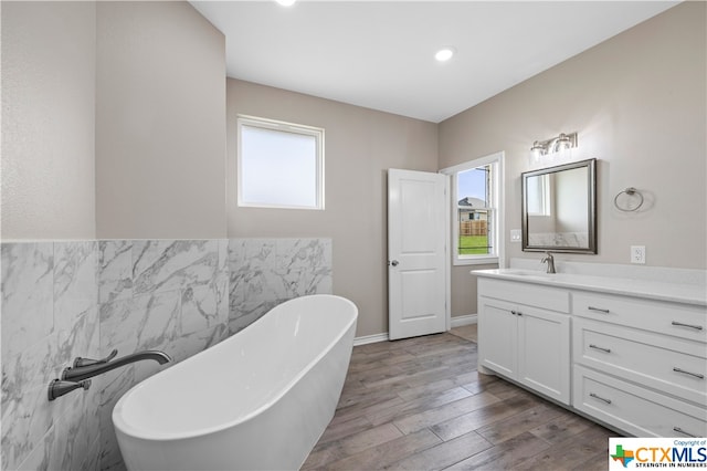 bathroom with vanity, a tub to relax in, tile walls, and wood-type flooring