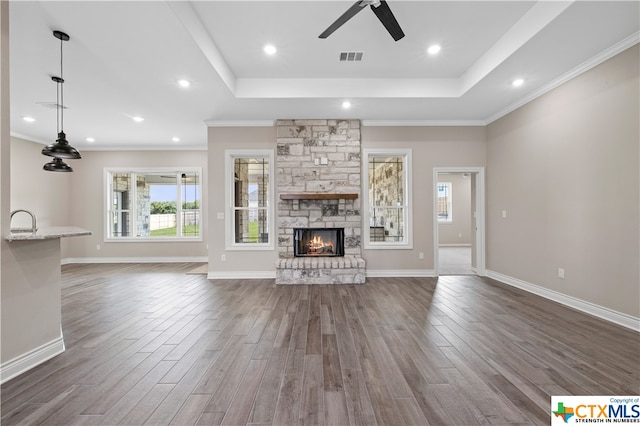 unfurnished living room featuring dark wood-type flooring, a fireplace, a tray ceiling, and ornamental molding