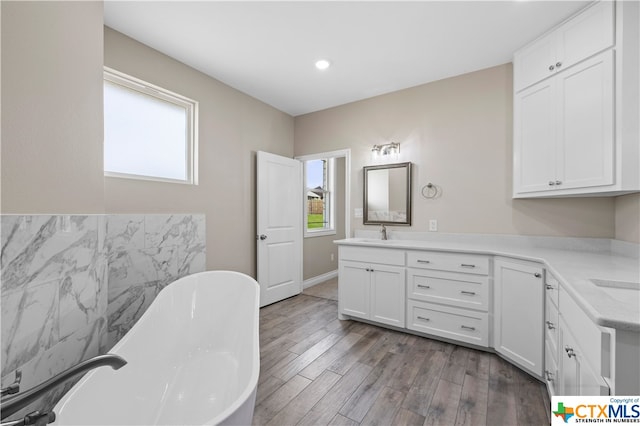 bathroom with a wealth of natural light, wood-type flooring, vanity, and a bathing tub