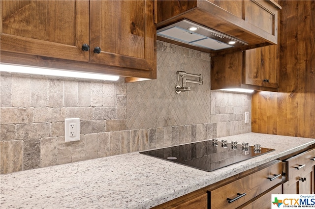 kitchen featuring backsplash, custom range hood, black electric stovetop, and light stone counters