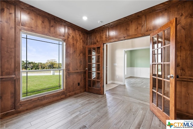 unfurnished room with ornamental molding, french doors, light hardwood / wood-style flooring, and wood walls