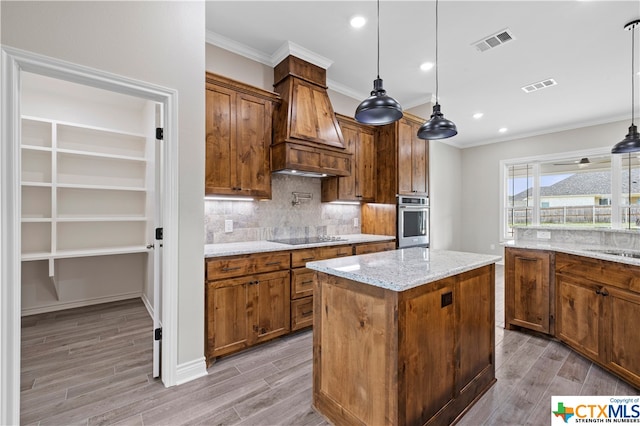 kitchen featuring hanging light fixtures, oven, light hardwood / wood-style flooring, a kitchen island, and premium range hood