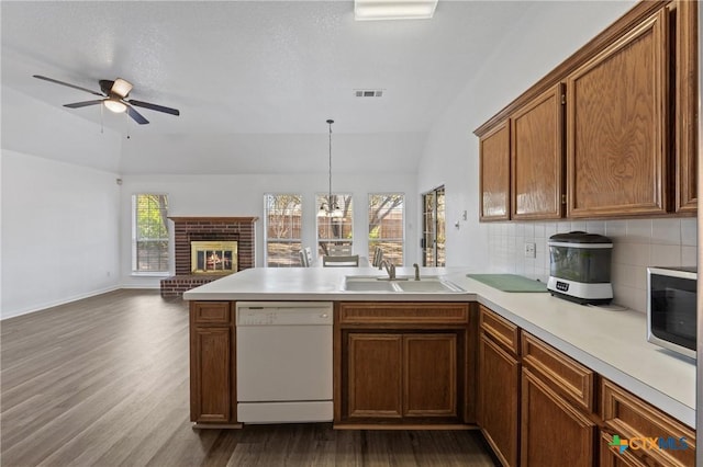 kitchen featuring pendant lighting, sink, white dishwasher, a brick fireplace, and kitchen peninsula