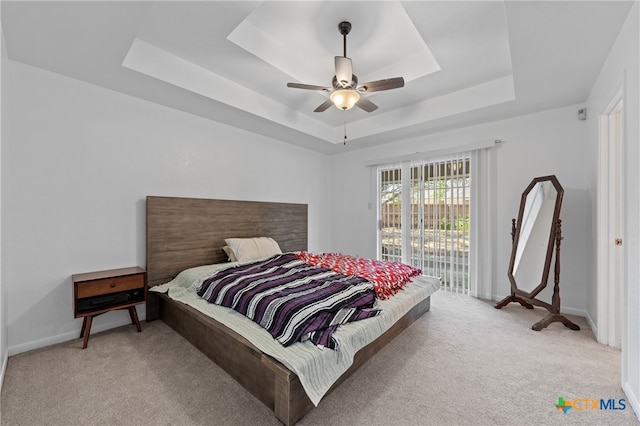 carpeted bedroom featuring ceiling fan, a tray ceiling, and access to exterior