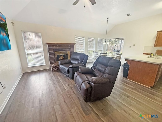 living room featuring vaulted ceiling, a brick fireplace, wood-type flooring, and ceiling fan