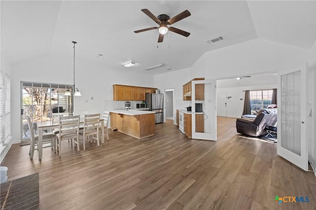 kitchen with ceiling fan with notable chandelier, high vaulted ceiling, decorative light fixtures, wood-type flooring, and stainless steel fridge