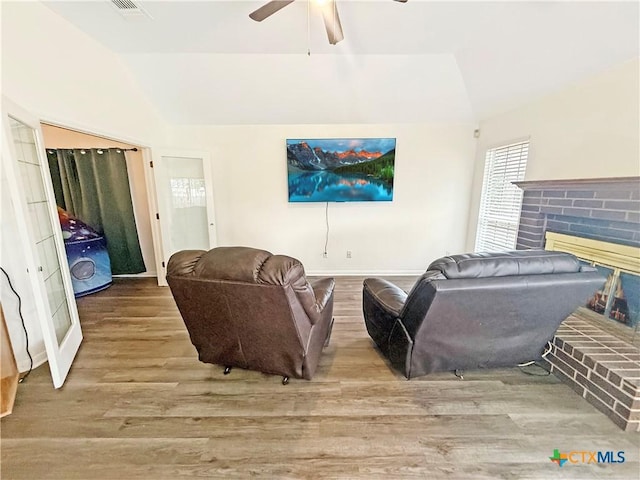 living room with ceiling fan, lofted ceiling, light hardwood / wood-style floors, and a brick fireplace