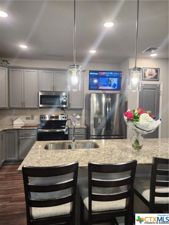 kitchen featuring light stone countertops, decorative light fixtures, stainless steel appliances, and sink