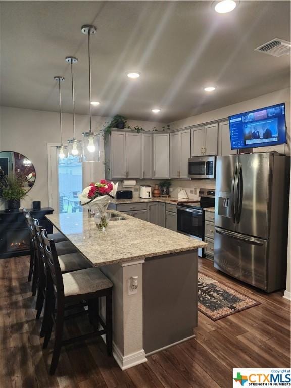 kitchen featuring stainless steel appliances, dark hardwood / wood-style floors, gray cabinets, and hanging light fixtures