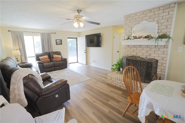 living room with ceiling fan, light hardwood / wood-style floors, a textured ceiling, and a brick fireplace